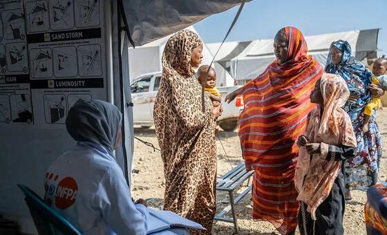 一名联合国人口基金的卫生工作者正在与阿布·纳贾难民营流动诊所的求诊妇女和儿童交谈。